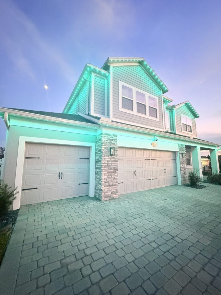 Home lit in teal green with a paver driveway and moon in Sanford, Florida