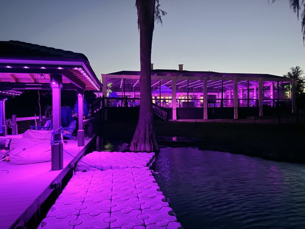 Boat dock and deck glowing pink and purple at dusk with the lit pool enclosure across the water in Windermere, Florida