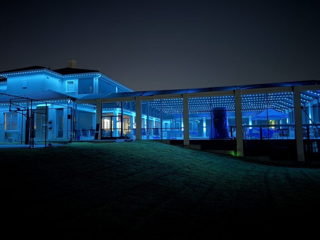 Home and screened pool enclosure lit in bright blue with track lighting and wall sconces on the enclosure columns in Windermere, Florida