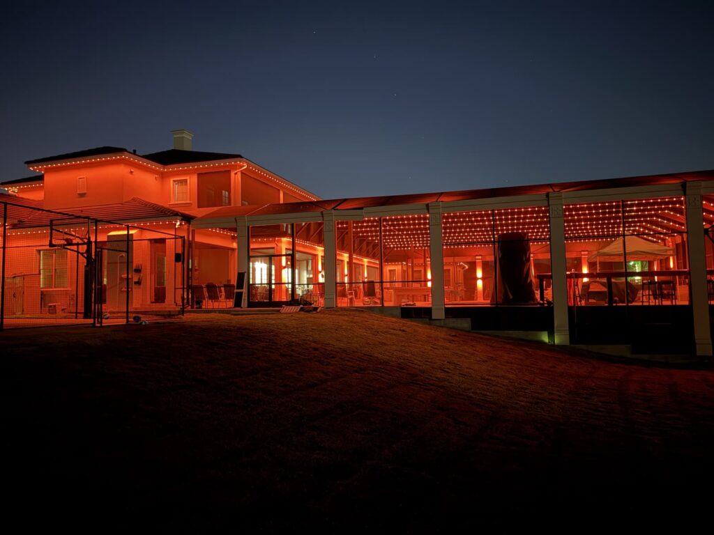 Home and screened pool enclosure glowing orange with track lighting grid across the enclosure ceiling in Windermere, Florida