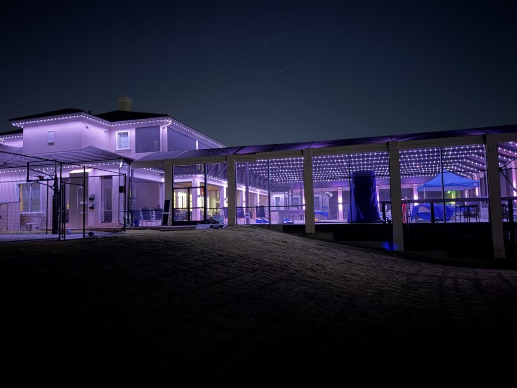 Home and screened pool enclosure lit in soft purple with white track lighting across the enclosure ceiling and roofline in Windermere, Florida