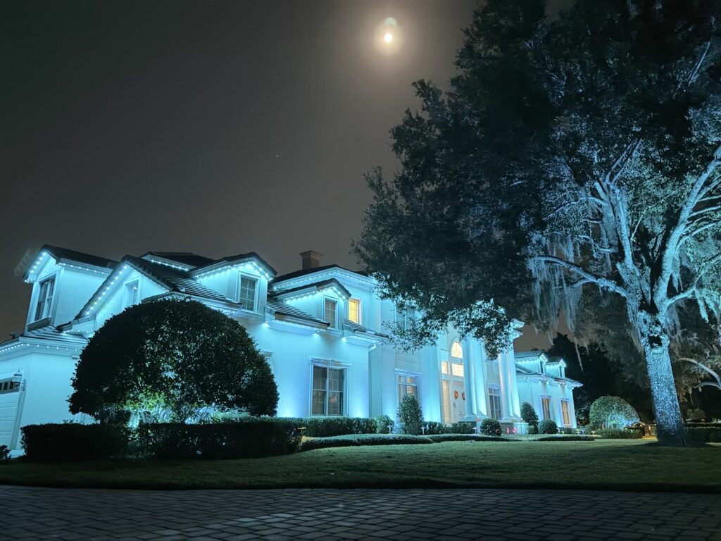 Home and oak trees washed in ice blue permanent outdoor lighting under a full moon in Windermere, Florida
