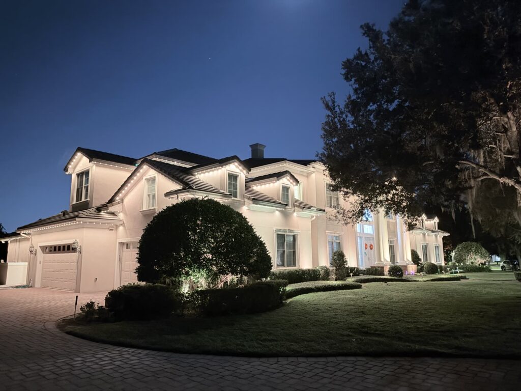 Large home with warm white roofline lighting and landscape uplighting at dusk in Windermere, Florida