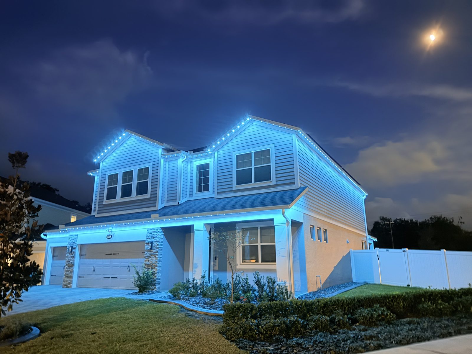 Two story home at night washed in continuous blue light from a Brighter Nights roofline system