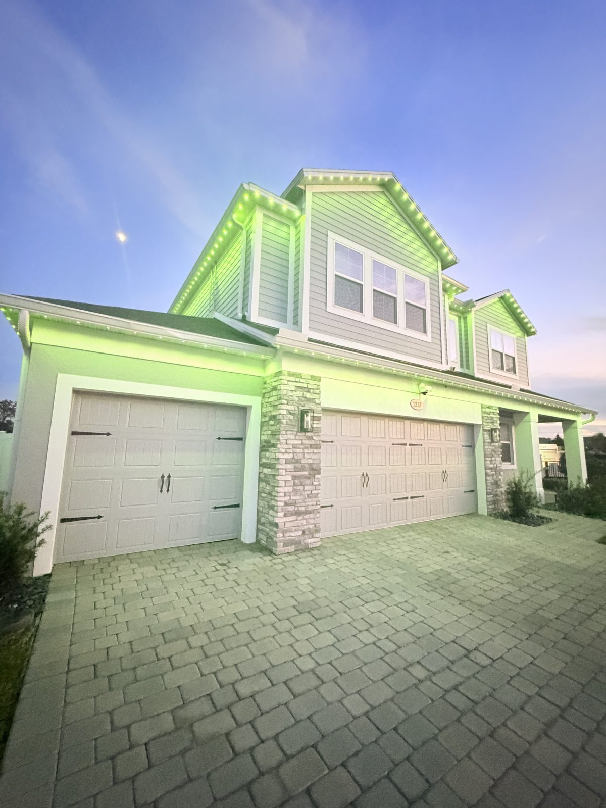 Two story home at dusk washed in continuous green light from a Brighter Nights roofline system