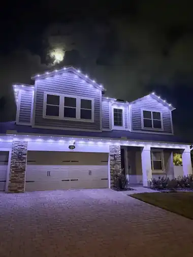 Home at night with cool white architectural downlights spaced along the soffit, one light on and three or four off