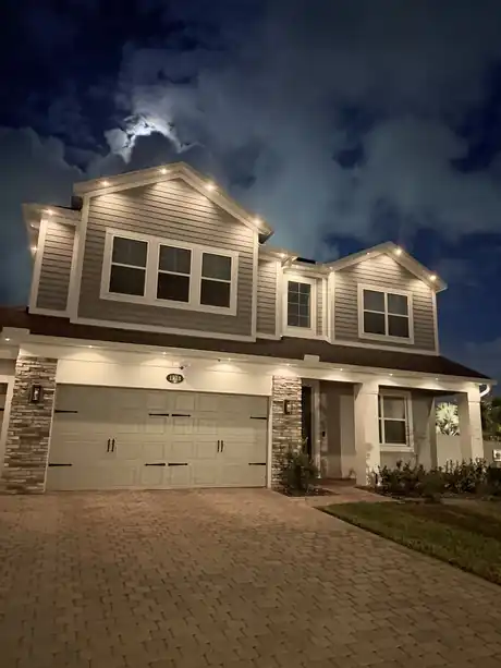 Two story home at night with warm white architectural downlights spaced along the soffit, one light on and three or four off