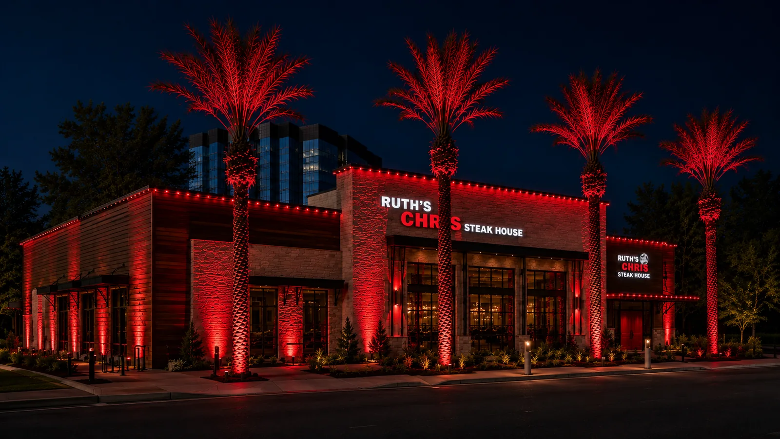 A restaurant exterior at night with its palm trees, columns and roofline all washed in the brand's signature red by Brighter Nights Lighting Technologies landscape and roofline lighting