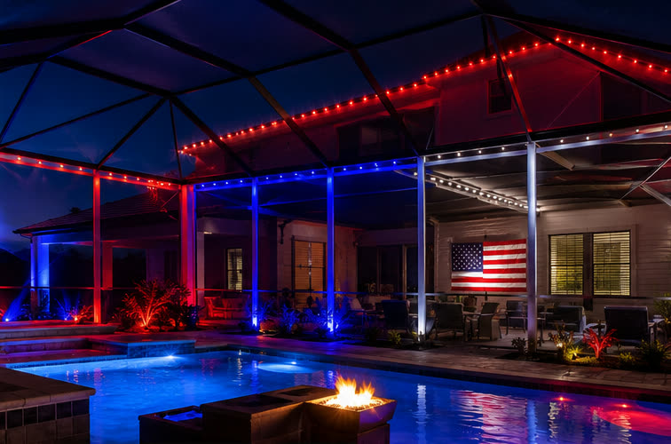 A screened pool enclosure lit red, white and blue with a US flag on the wall for the Fourth of July