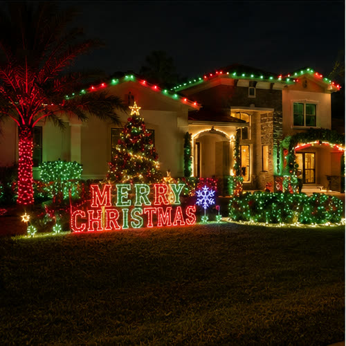 A home lit red and green for Christmas with a lit tree and a MERRY CHRISTMAS yard display