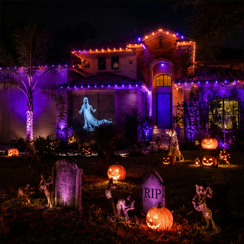 A home washed in orange and purple roofline and wall lighting for Halloween, with a ghost projection and pumpkins