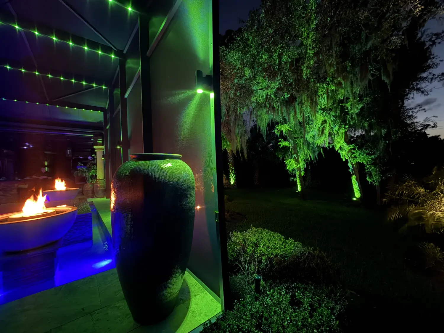 Pool enclosure sconces and landscape uplights in emerald green across the oaks and screen wall