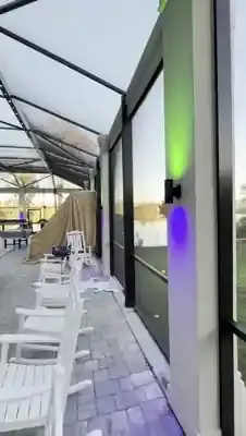 Solid brass sconce mounted on a pool enclosure post in daylight, showing saturated color output against the bronze frame while the pool enclosure track lighting runs overhead