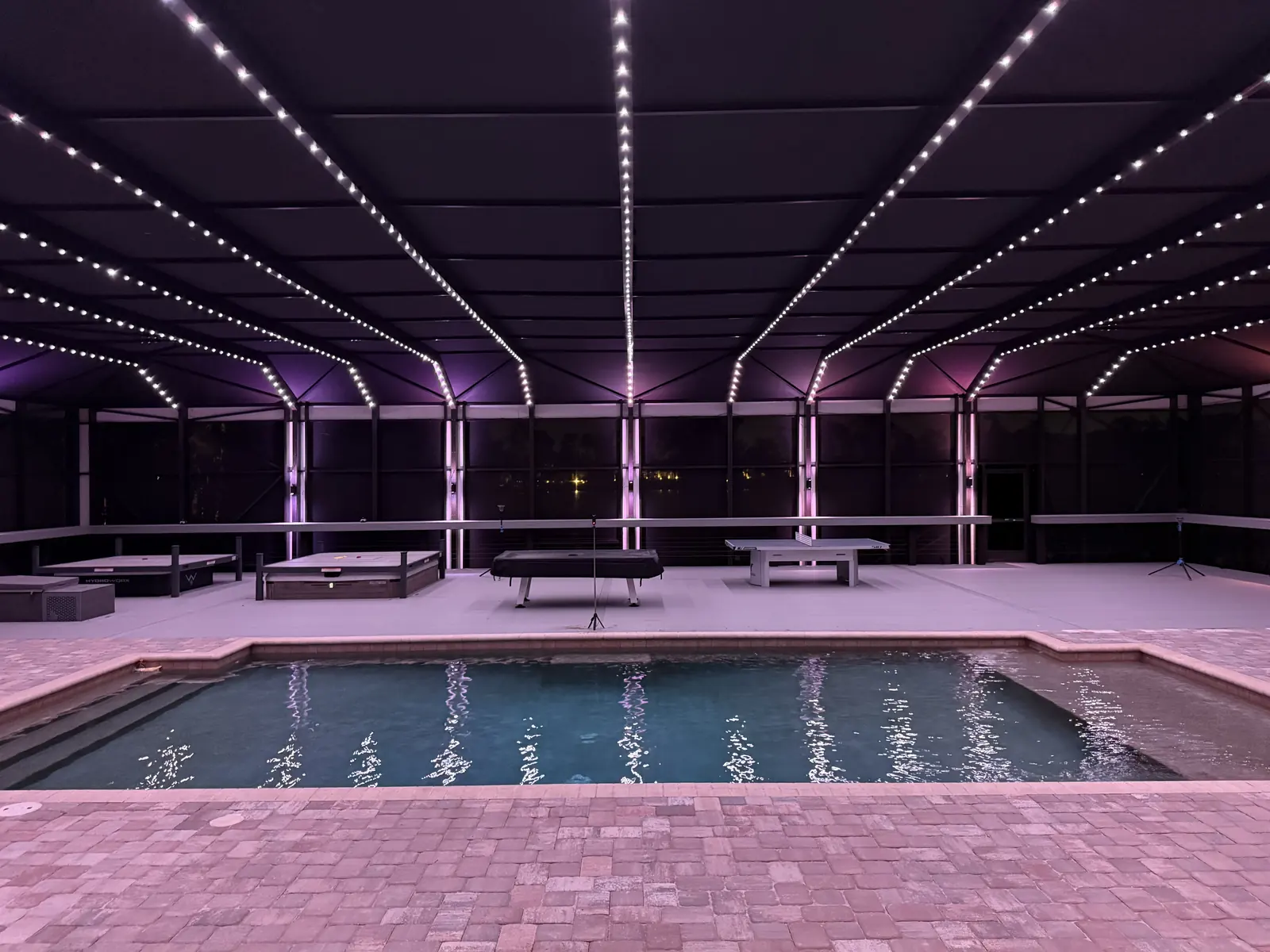 The pool enclosure at night with BNLT track lighting on &mdash; every beam and column lit